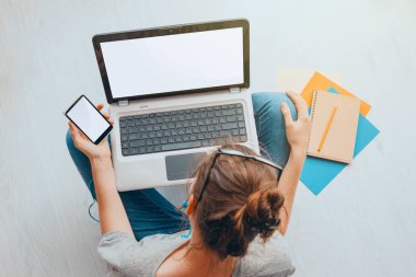 Dizüstü bilgisayar ile katta oturan ve telefon tutarak genç kadının Üstten Görünüm