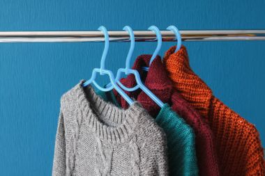 Warm woolen sweaters hanging on hangers clipart