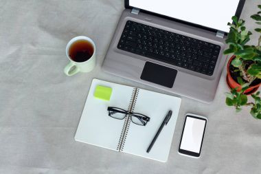 Konfor işyeri üstten görünüm. Dizüstü bilgisayar, boş ekran, defter, telefonu ve fincan çay ile Designer Danışma
