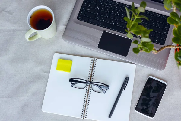 Konfor işyeri üstten görünüm. Dizüstü bilgisayar, boş ekran, defter, telefonu ve fincan çay ile Designer Danışma