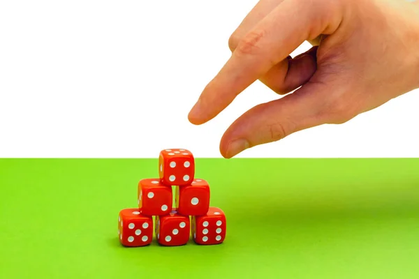 Hand reaches red dice in a pyramid on green background — Stock Photo, Image