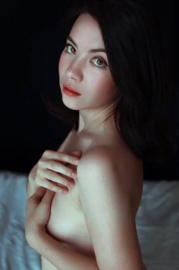 Yatak, büyüleyici gözleri iri, çıplak omuz ve sırt elleri onun göğüsler kapsayan oturmuş poz şehvetli genç kadın