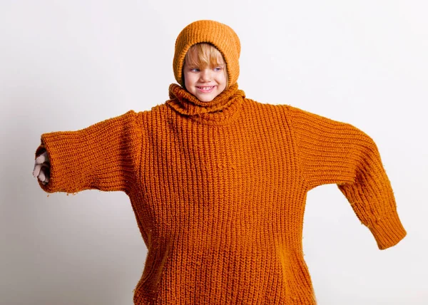 Очаровательная маленькая девочка, милый малыш в вязаной шляпе и огромном оранжевом свитере, играющий и веселый улыбающийся над студийной серой стеной . — стоковое фото