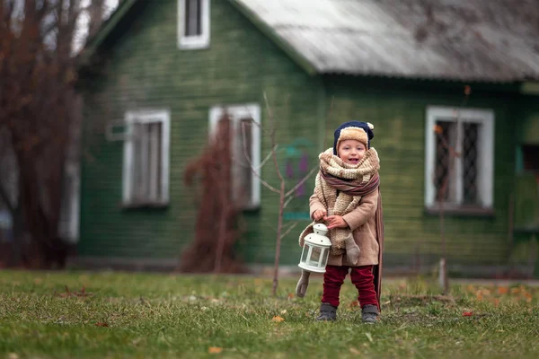 Kırsalda eğlenen sevimli küçük bir çocuk. Bebek dışarıda klasik el feneriyle oynuyor. Arka planda sonbahar dönemi ahşap evi.. — Stok fotoğraf