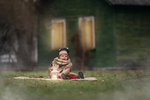 Kırsalda eğlenen sevimli küçük bir çocuk. Bebek dışarıda klasik el feneriyle oynuyor. Arka planda sonbahar dönemi ahşap evi.. — Stok fotoğraf
