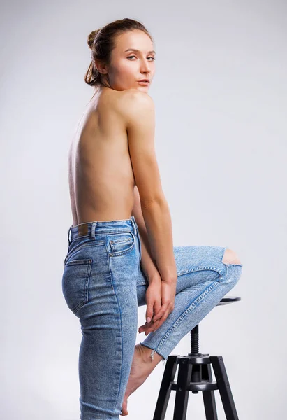 Imagen de la hermosa mujer en topless en jeans que cubren los pechos con las manos sobre fondo gris — Foto de Stock