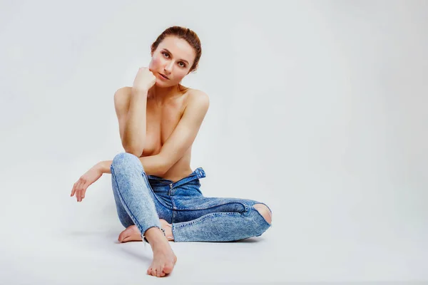 Foto van mooie topless vrouw in jeans zittend op vloerbedekking borsten met handen poserend in de studio op grijze achtergrond — Stockfoto