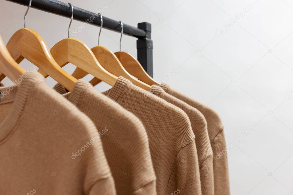 Warm woolen sweaters beige color hanging on hangers