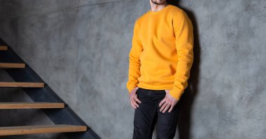 Sarı kazaklı ya da uzun kollu bir adam. Evdeki duvarın yanındaki merdivenlerde duruyor. Yazdırma için model