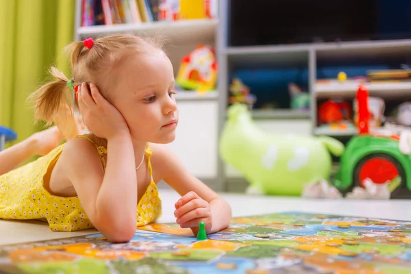 Board game concept. Little kid girl play in board game at home sitting on a wooden floor. Board game field, many figures.