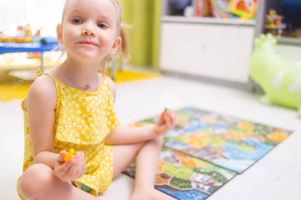 Board game concept. Little kid girl play in board game at home sitting on a wooden floor. Board game field, many figures.