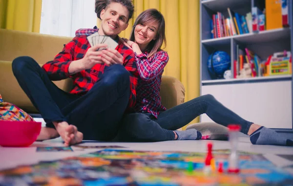 Board game concept- friends spend time together. Board game field, figures, dice, coins and sandglass. Two people holding cards funny play and hug