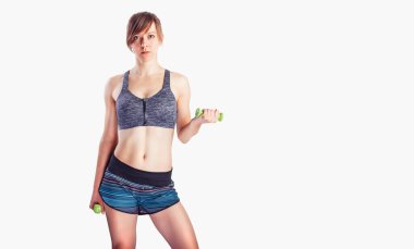 Sportif kadın egzersizleri gri arka planda dambıllarla yapıyor. Stüdyoda spor giyim bölümünde kaslı bir kadının fotoğrafı.