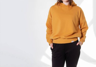 Boş kazak ve spor pantolon giyen genç bir kız. Metin mesajınız veya tanıtım içeriğiniz için penceredeki gri duvar gölgesi ışığı