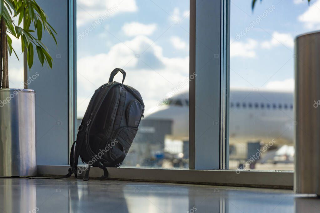 Backpack at airport near the window. Airplane, blue sky, waiting in departure lounge area, hall, lobby, vacation trip