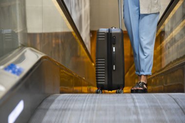 Kız havaalanında tatil gezisi sırasında bavuluyla yürüyen merdivende kıvranıyor. Seyahat, transfer, havaalanında beklemek.