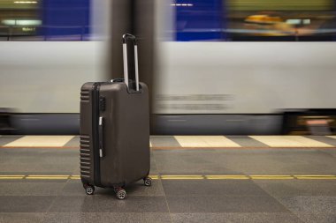 Hareket halindeki trenin yanındaki tren istasyonunda bagajlar tekerleklerin üzerinde. Seyahat sırasında istasyonda beklemek ya da valizlerle tatil yapmak