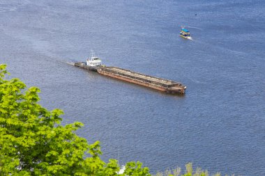 A tug boat hauls a large, empty barge down wide Dnipro river dirung sunny day. Seafaring, navigation on river