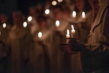 İnsanlar kilisedeki geleneksel dini kıyafetlerde mumlara dokunuyorlar. Lucia Günü, İsveç Kutlaması