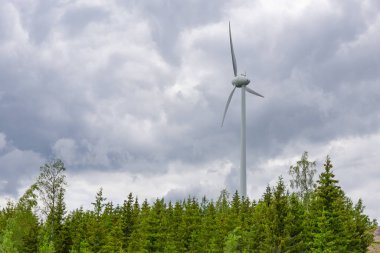 Yeşil ormanın ortasında, gri bulutların altında tek bir rüzgar türbini. Rüzgar çiftliği, rüzgar santrali