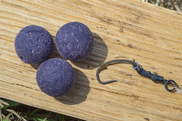 Ameixa de amoreira boilies roxos com gancho de pesca. Equipamento de pesca para carpas, equipamento boilie, perto do lago em um pedaço de madeira — Fotografia de Stock