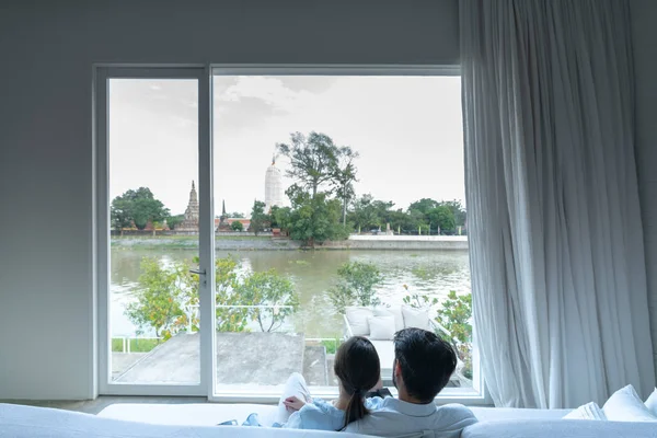 Coppia seduta sul divano letto e guardando attraverso la finestra nel loro nuovo appartamento con fantastica vista sul fiume / casa in movimento / obiettivo relazione — Foto Stock