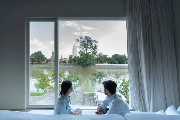 Coppia seduta sul divano letto e guardando attraverso la finestra nel loro nuovo appartamento con fantastica vista sul fiume / casa in movimento / obiettivo relazione — Foto Stock