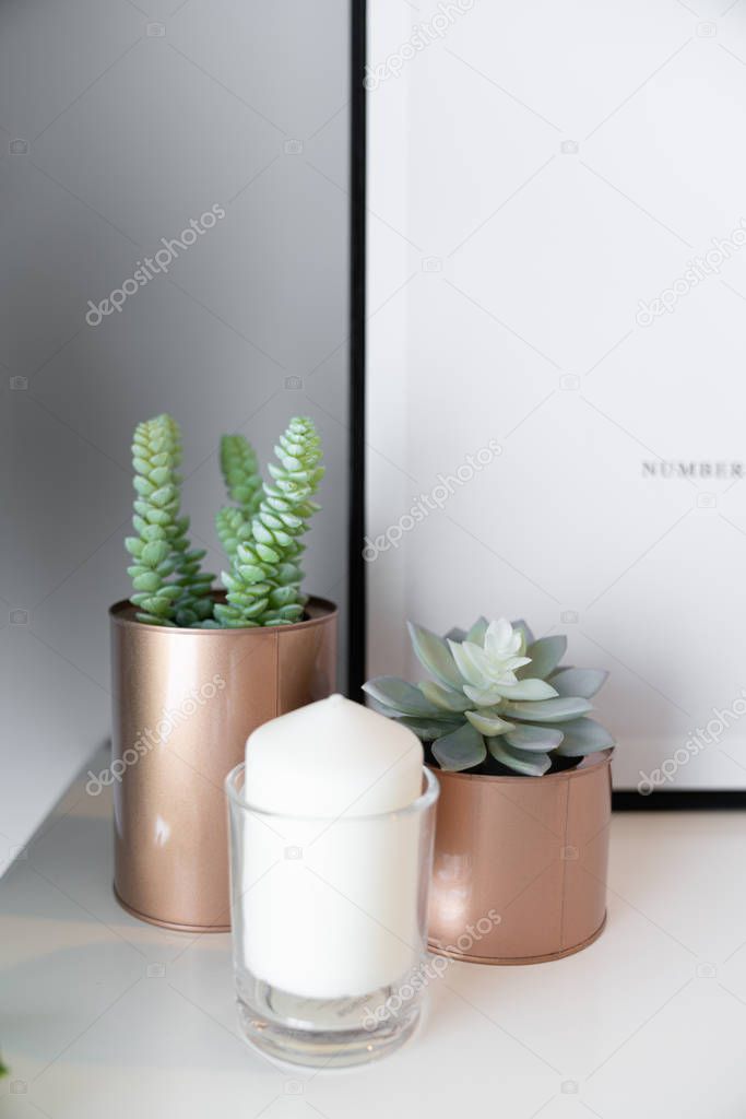 Close up  copper vase  with artificial plant inside and white candle in glass on cream spray-painted working table with  gray painted wall in the background /apartment interior /copy space