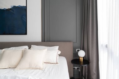 Konforlu yatak odası köşesi modern kahverengi kumaştan yatak başlığı ve altın lambalı rahat yastıklar ve modern fiş arka planda gri renkli klasik duvar ve iç tasarım dekorasyonu üzerine kurulur.