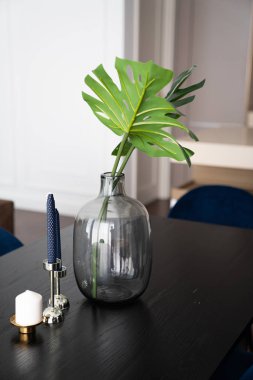 Mavi mum tutacağı olan cam vazodaki suni bitki, siyah ahşap yemek masasının üzerinde minimum modern tarzda bir daire / konut konsepti / kopyalanmış yer alıyor.