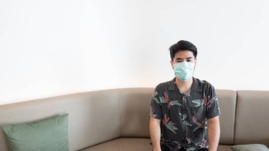 Kanepede oturan ve ameliyat maskesiyle fotokopi çeken adamlar.