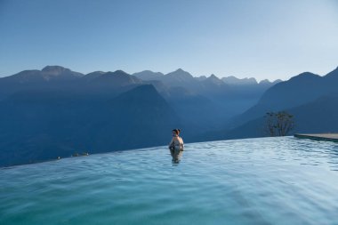 Sonsuz yüzme havuzunda dinlenen seksi kadın lüks tatil / tatil konseptinde çarpıcı dağ manzaralı.