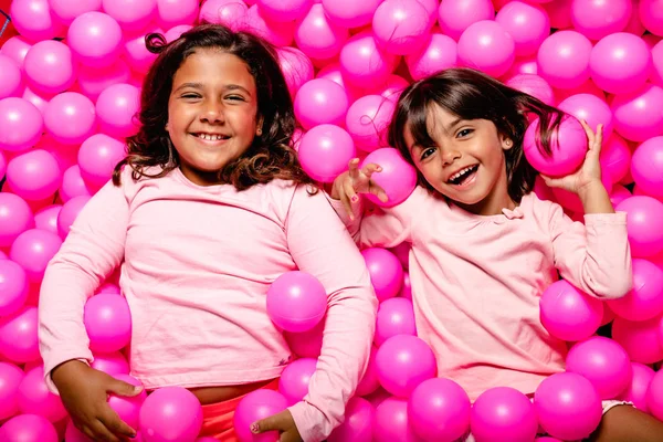Δύο μικρά κορίτσια χαμογελούν και παίζουν στην πισίνα με τις ροζ μπάλες — Φωτογραφία Αρχείου