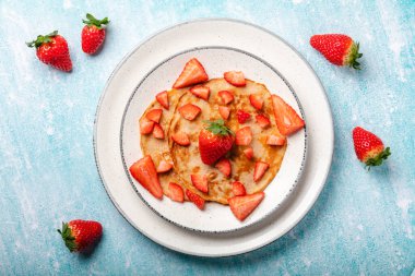 Mavi ahşap arka planda taze çilekli krepler.