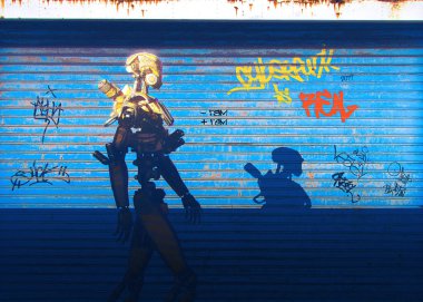 Üzerinde grafitti olan mavi bir duvarın yanında yürüyen bir Sayborg. 