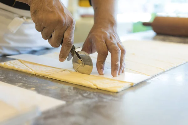 man at kitchen cutting dough for croissant