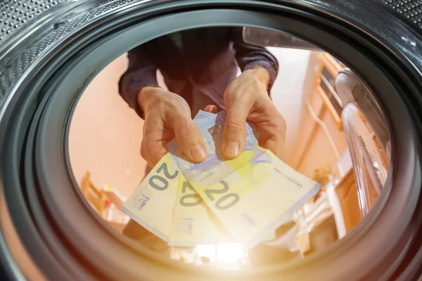 a man throws money euro into a washing machine, the concept of illegal entrepreneurship, money laundering, and breaking the law and tax evasion