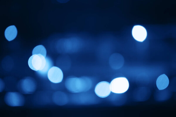 Night city with lights and headlights of cars and brake lights, abstract photo with bokeh and blur effect toned in color classic blue, the trend of the year 2020