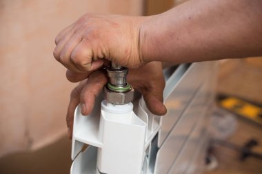 Dairedeki radyatörün değiştirilmesi, su tesisatı. Bir adam ısıtma bataryalarının montajını yapıyor.