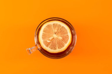 Cup of Hot tea with lemon in a ceramic mug on a colored orange background