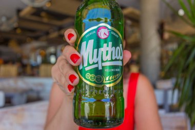 FALIRAKI, RHODES, GREECE - JULY 13, 2019: Girl holding a bottle of Greek beer Mythos in a restaurant on the street in the afternoon