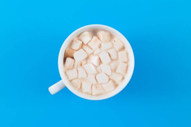 Hot cocoa in a white mug with marshmallow on a colored background in the middle