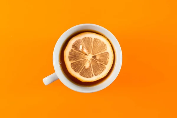 Cup of Hot tea with lemon in a ceramic mug on a colored orange background