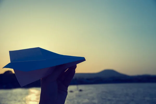 自然の中で指 日没や夜明けに女性の手の中に空と海の背景に紙飛行機 夢と成功への欲求の概念  — 無料ストックフォト