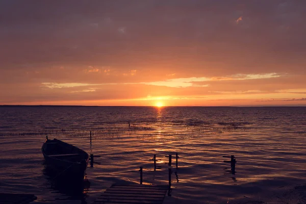 在美丽的落日下 一艘木制的渔船缓缓地在一个大湖面的浪花上摇曳 夕阳西下 水中映出美丽的天空和云彩 — 图库照片