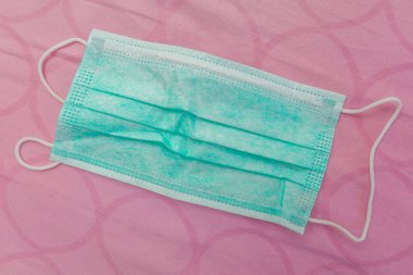 Yatağın üzerindeki çarşafta Coronavirus 'tan korunmak için tıbbi maskeli pelüş ayı, sevdiklerine ve çocuklarına bakma kavramı