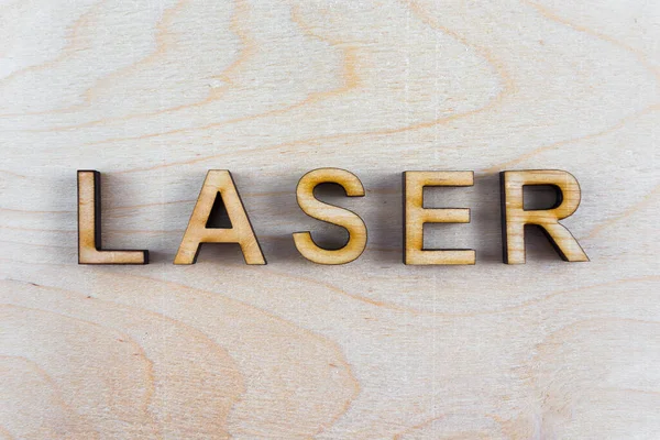 The word laser from the laser-cut plywood on wooden background