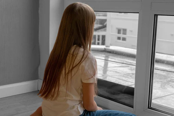 Triste chica adolescente mirando la lluvia cayendo por una ventana en casa o en el hotel . — Foto de Stock