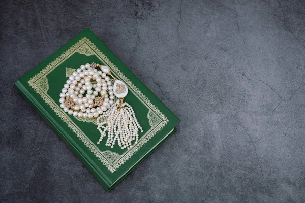 Μουσουλμανική ισλαμική πίστη έννοια Κοράνι βιβλίο, λευκό κομπολόι με την επιγραφή Αλλάχ. γκρι σκούρο τσιμέντο φόντο. διάταξη και χώρος για κείμενο — Φωτογραφία Αρχείου