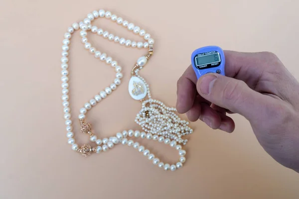 Hand counter. Tally counter in the hands of a man on a background of rosarie with the inscription Allah. Used by muslims in worship especially in holy Ramadhan